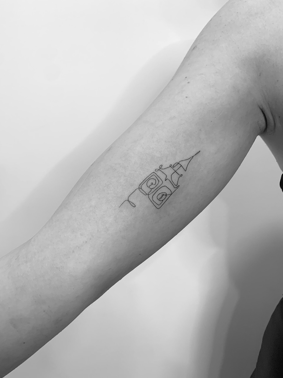 Fine line tattoo of a clock tower drawn in one continuous line on an upper arm