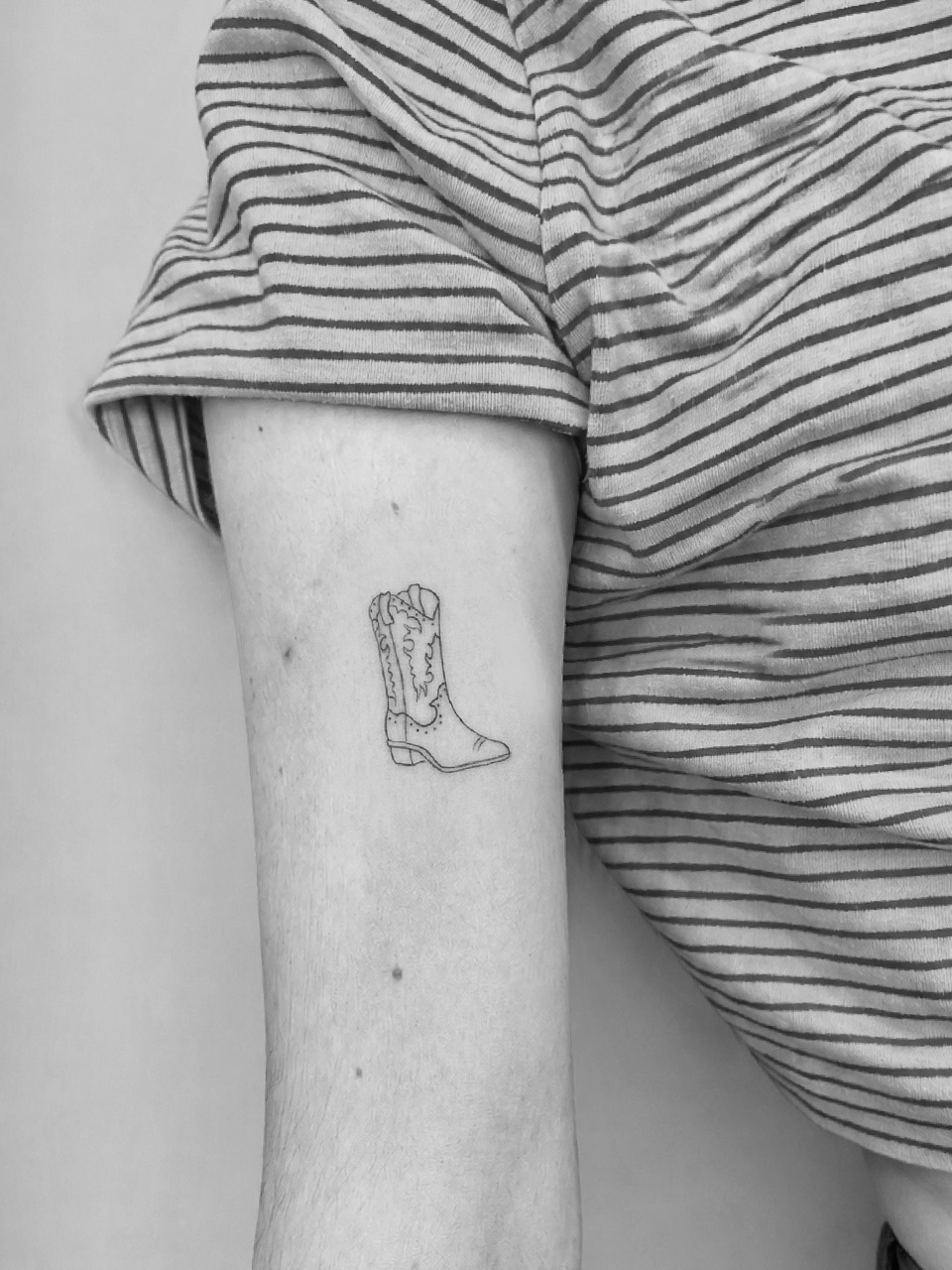Fine line tattoo of a cowboy boot on an upper arm