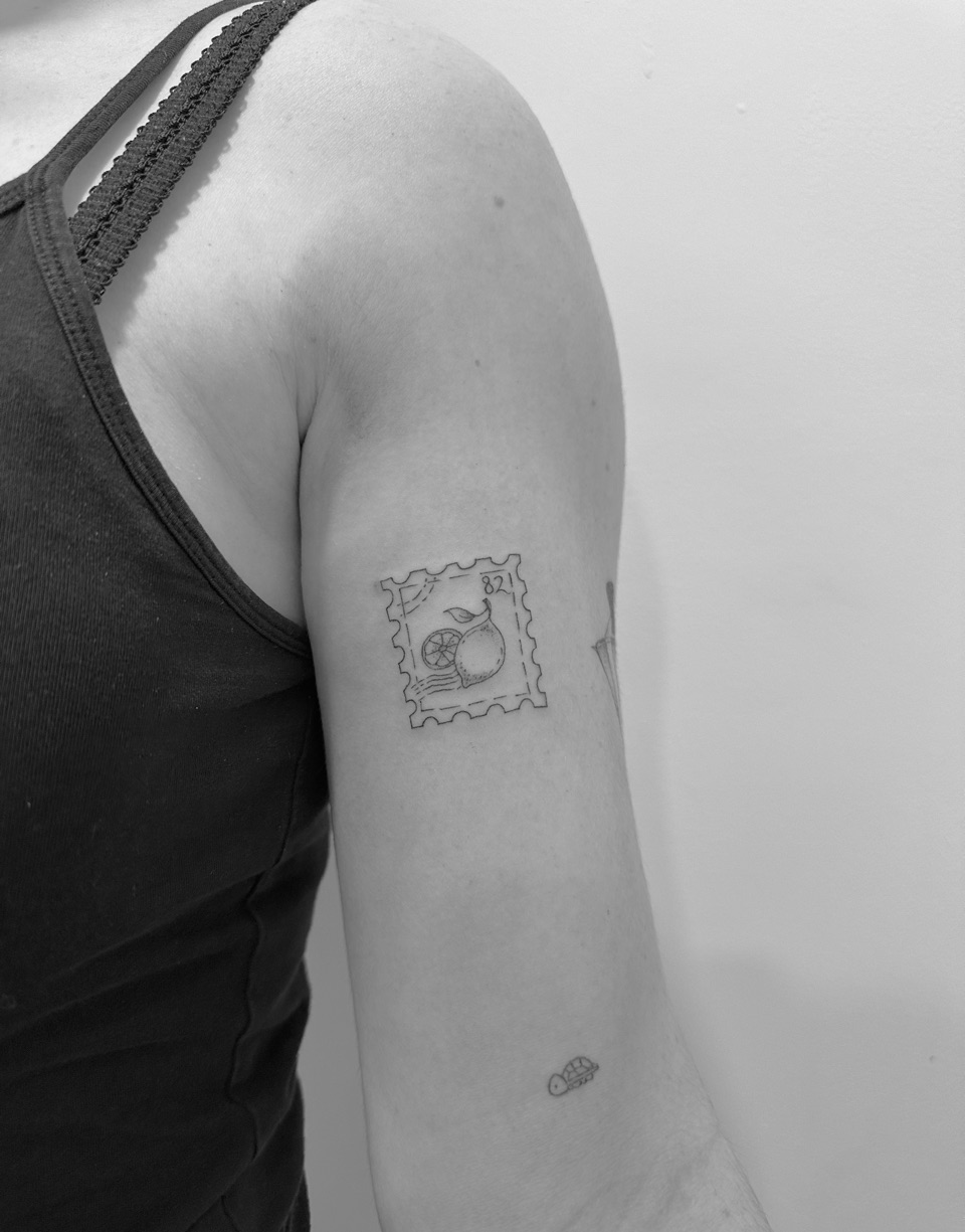 Fine line tattoo of a postage stamp with a lemon and a lemon slice, with the number 82