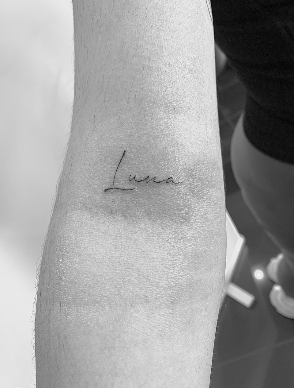 Fine line tattoo of the name Luna in handwritten script on a forearm