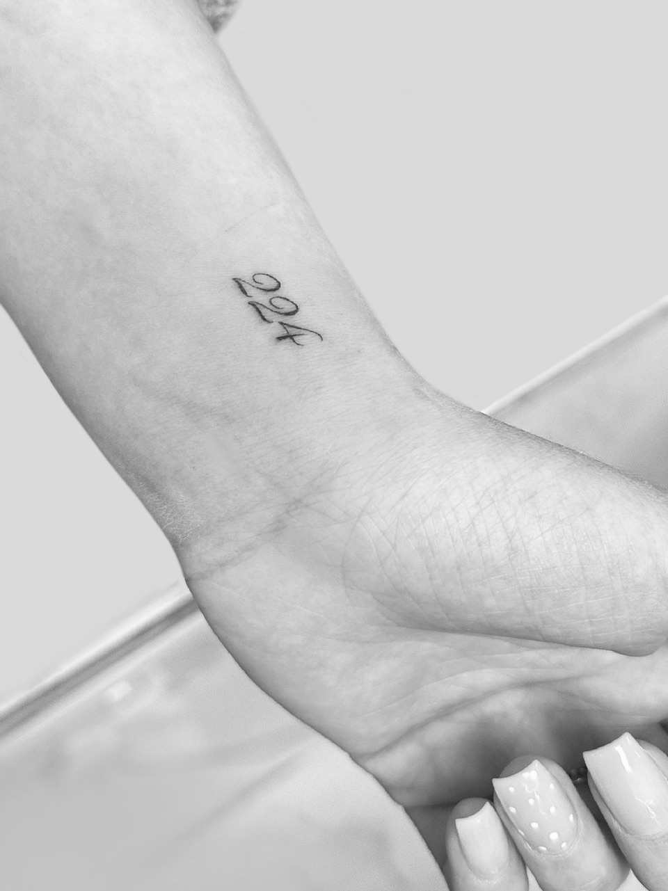 Fine line tattoo of small handwritten numerals on a wrist