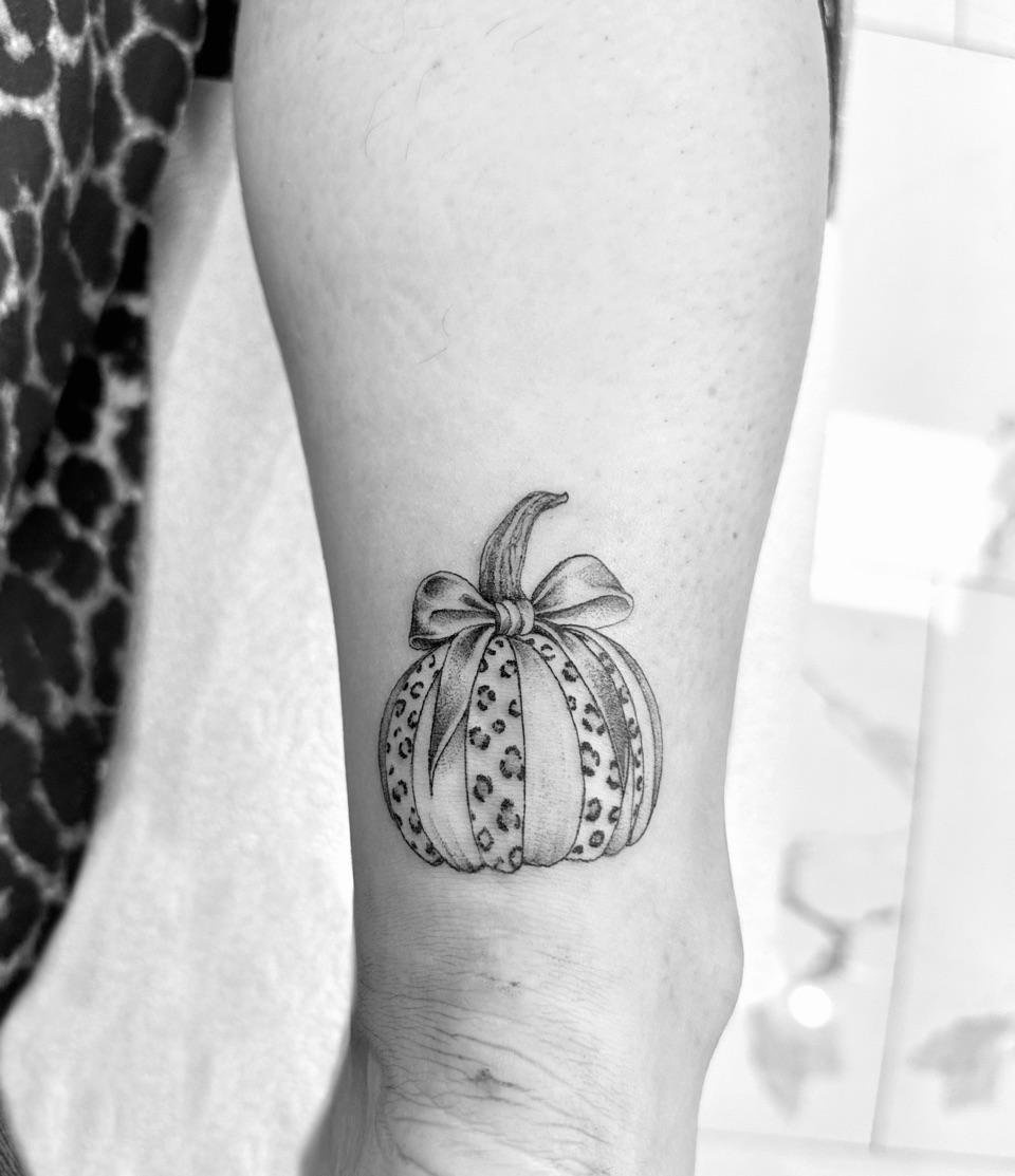 Tattoo of a pumpkin with leopard print stripes and a bow on its stem, on the back of a lower leg