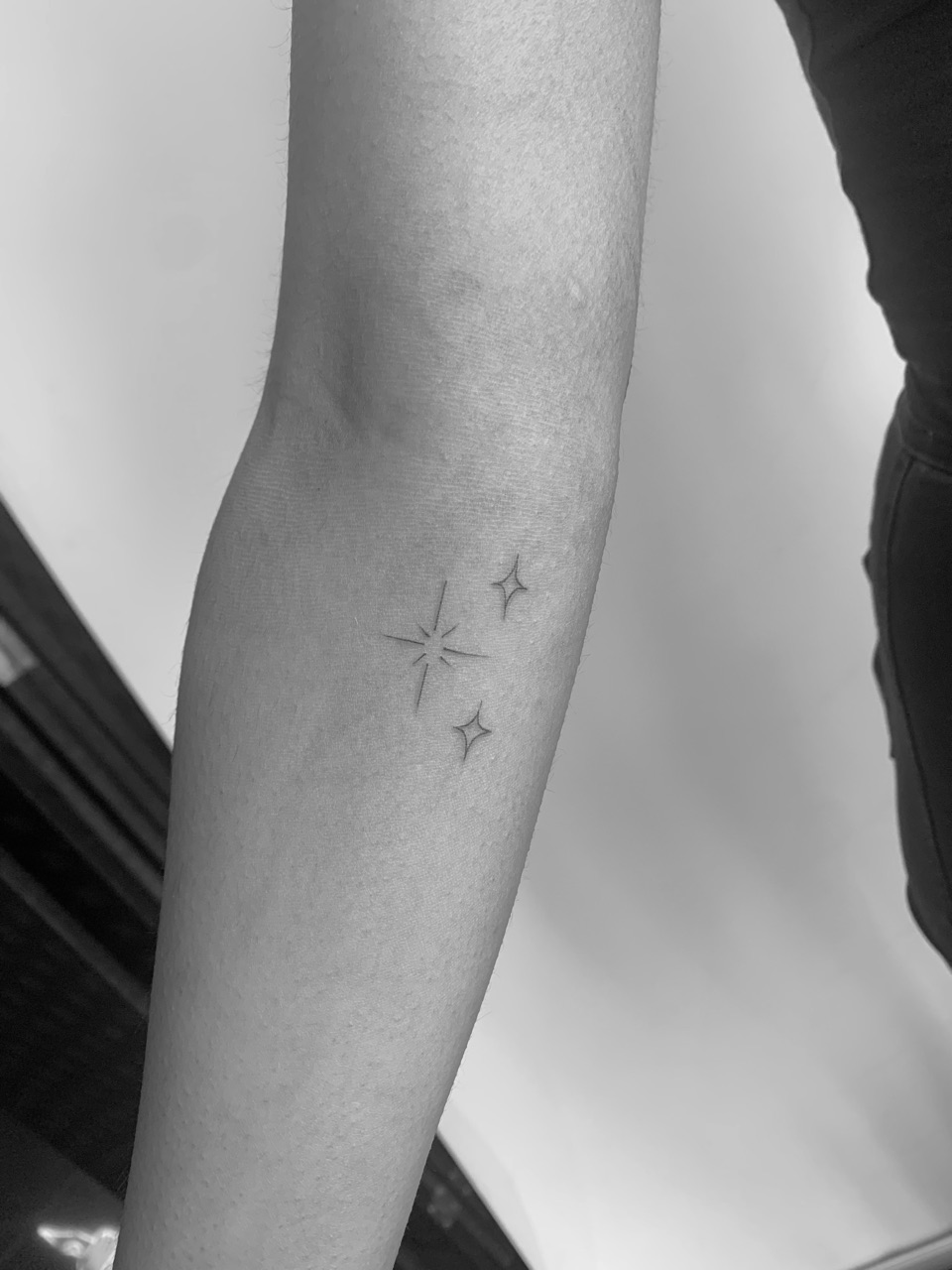 Fine line tattoo of a sparkle and two small stars on a forearm