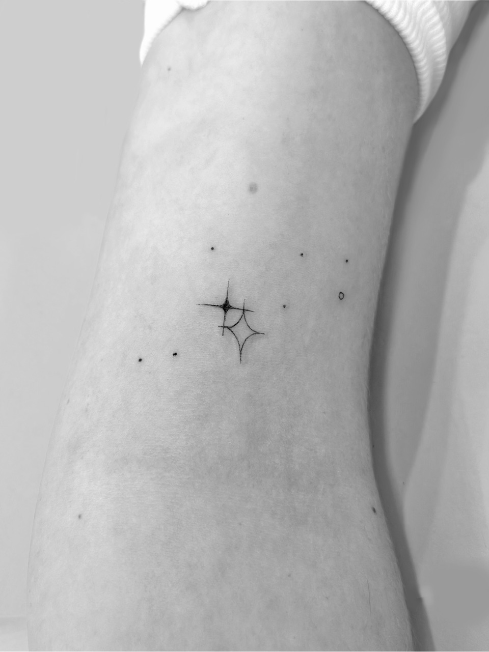 Fine line tattoo of two small stars surrounded by tiny dots